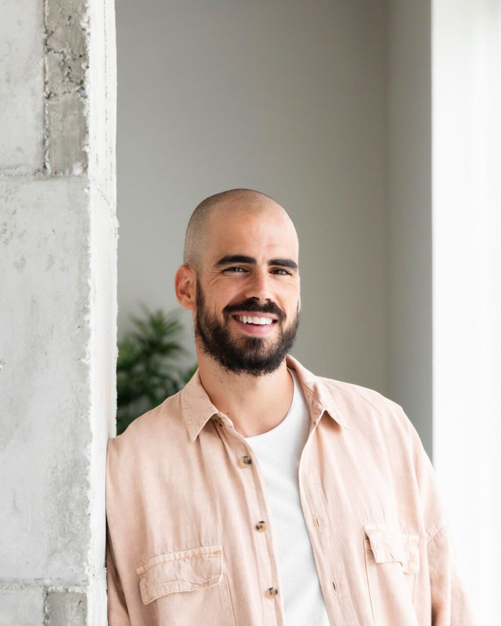 A smiling man leaning against a gray wall